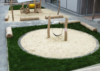Kreisrunde Sandfläche mit Mini-Schaukel im Rasen